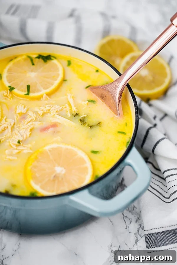 A beautiful blue Dutch oven filled with simmering Greek Lemon Chicken Soup, being expertly stirred with a gleaming metal serving spoon.