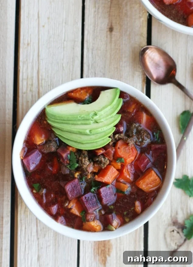 A white bowl of hearty AIP Instant Pot Chili, elegantly garnished with fresh sliced avocado, resting beautifully on a rustic wooden table.