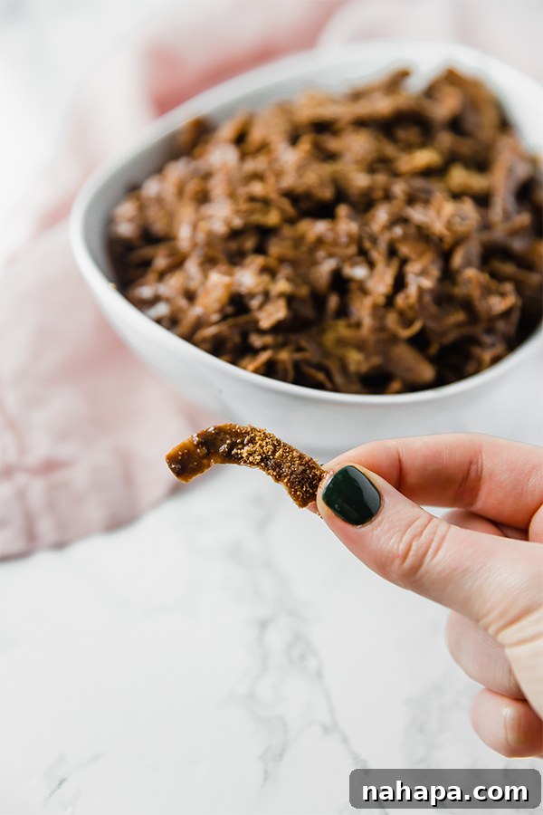 A white bowl filled with paleo coconut puppy chow with a hand holding one piece of puppy chow out in front, inviting you to try it.
