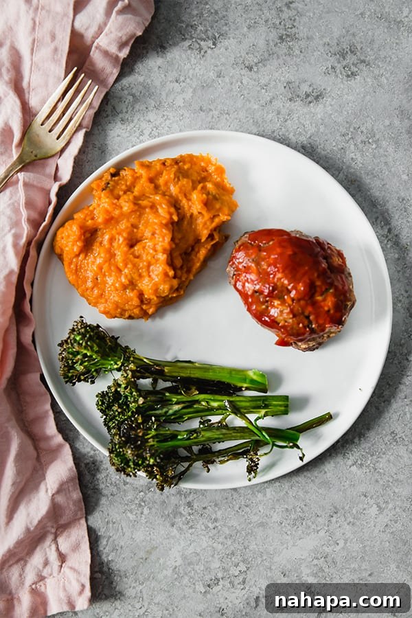 A white plate with mashed sweet potato, roasted broccolini, and a slice of meatloaf on it.