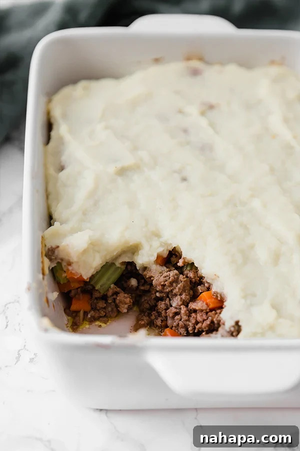 Comforting Cauliflower Shepherds Pie (Paleo, Whole30, AIP) 3 A casserole dish brimming with Cauliflower Shepherd's Pie, with one serving elegantly scooped out, revealing layers of savory meat and fluffy cauliflower.