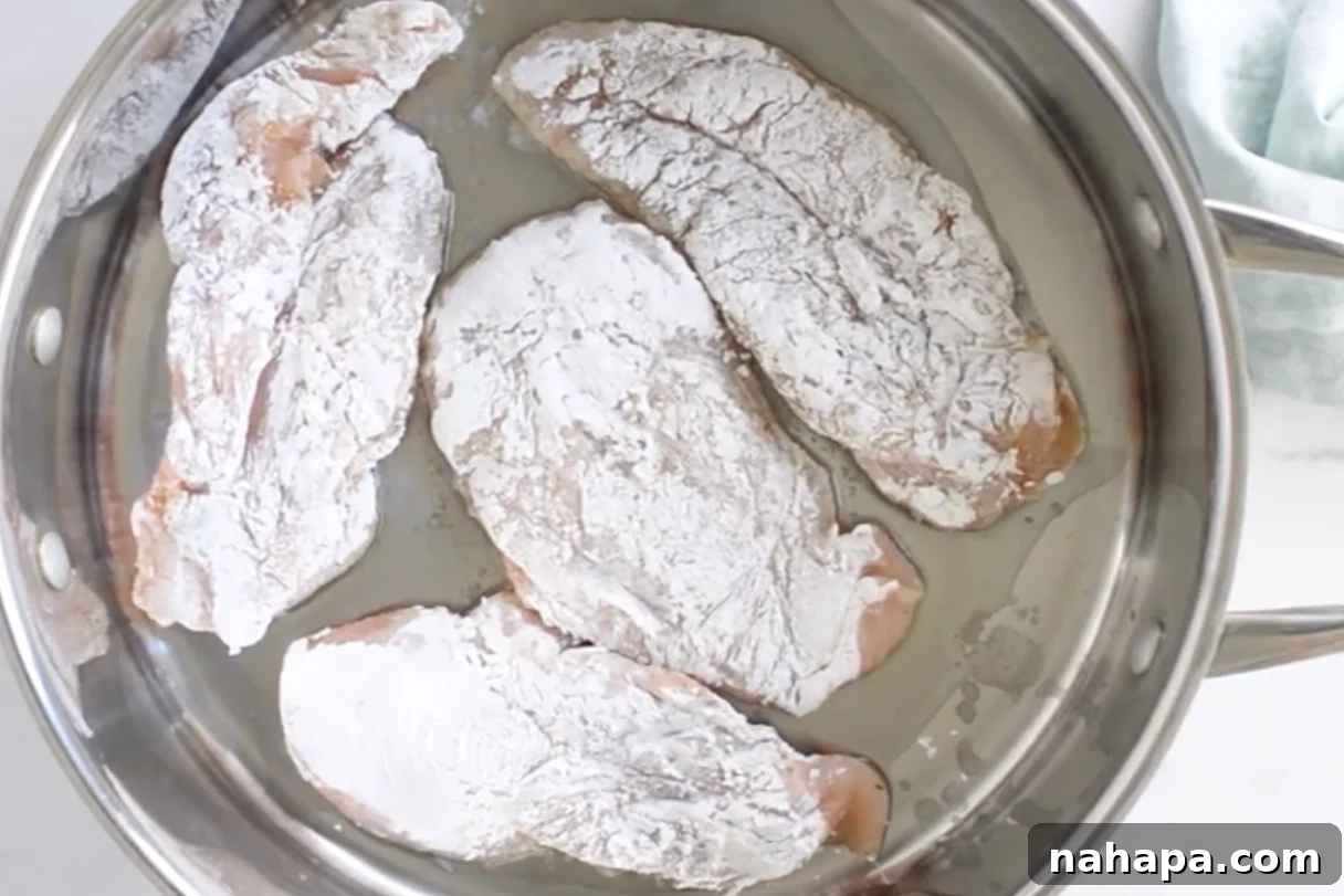 Arrowroot-coated chicken cutlets searing in hot oil in a pan until golden and crispy.