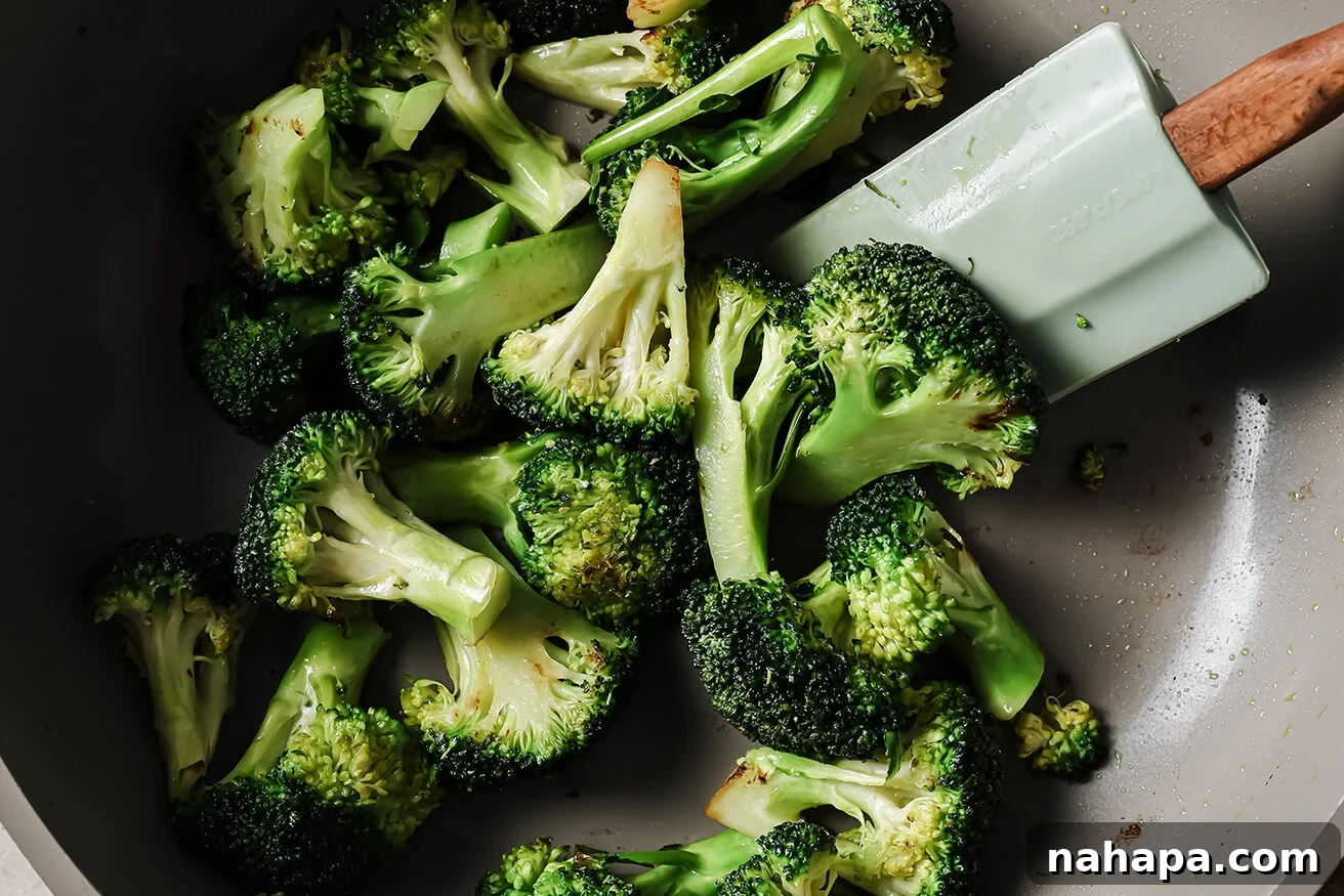 Broccoli florets being cooked in a pan with a spatula.