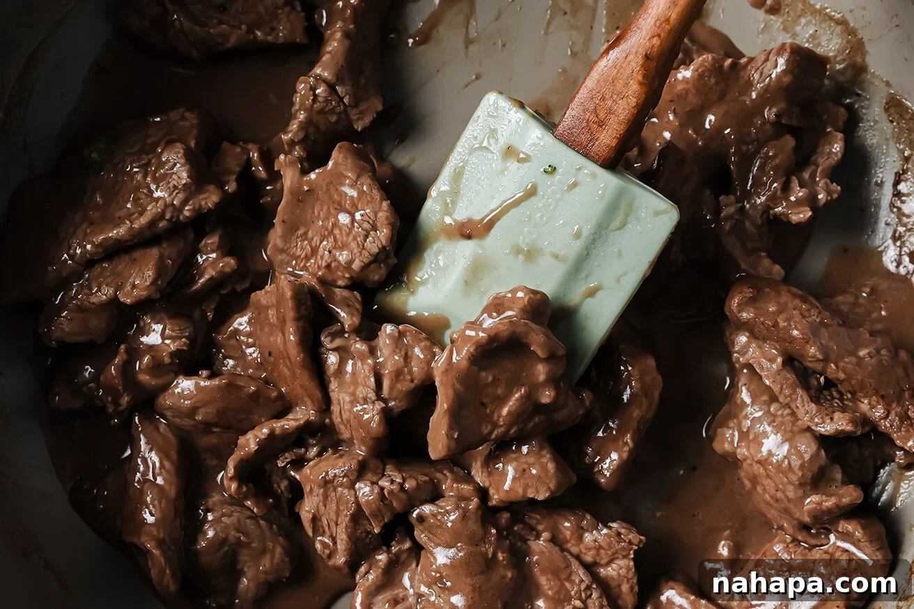 Mongolian beef cooking in a pan with sauce. 