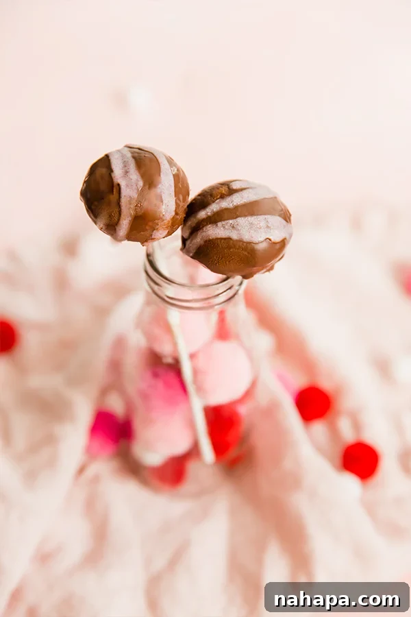 AIP and Gluten-Free No-Bake Paleo Cake Pops 4 Variety of no-bake cake pops on lollipop sticks, some with chocolate coating, some with pink drizzle.