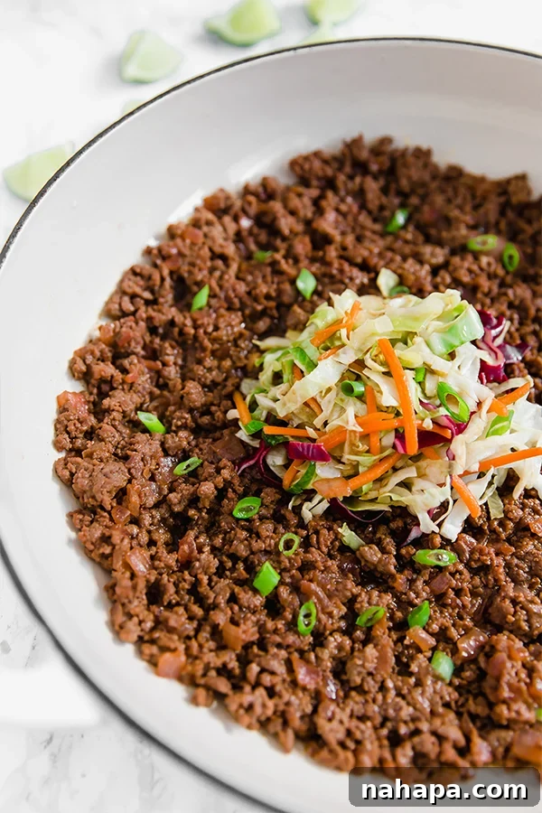 A close-up of Asian Sloppy Joe in a white skillet, garnished with fresh green onions.