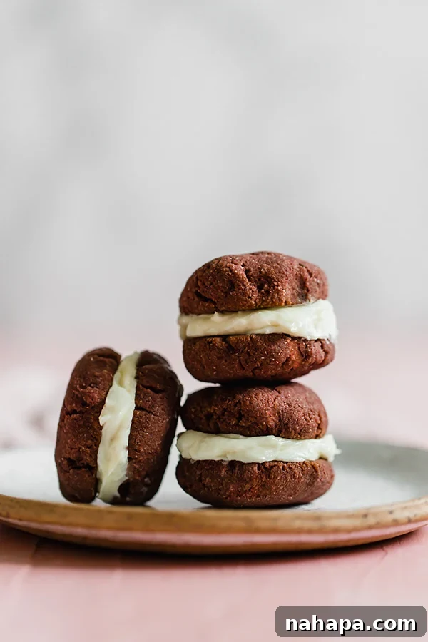 A stack of finished Red Velvet Whoopie Pies with a creamy filling, showcased on a wooden board.