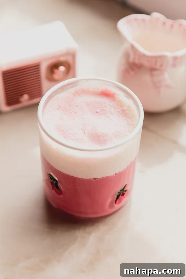 Two glasses of pink beet latte, one garnished with cinnamon, on a wooden board with fresh beet slices and cinnamon sticks scattered around.