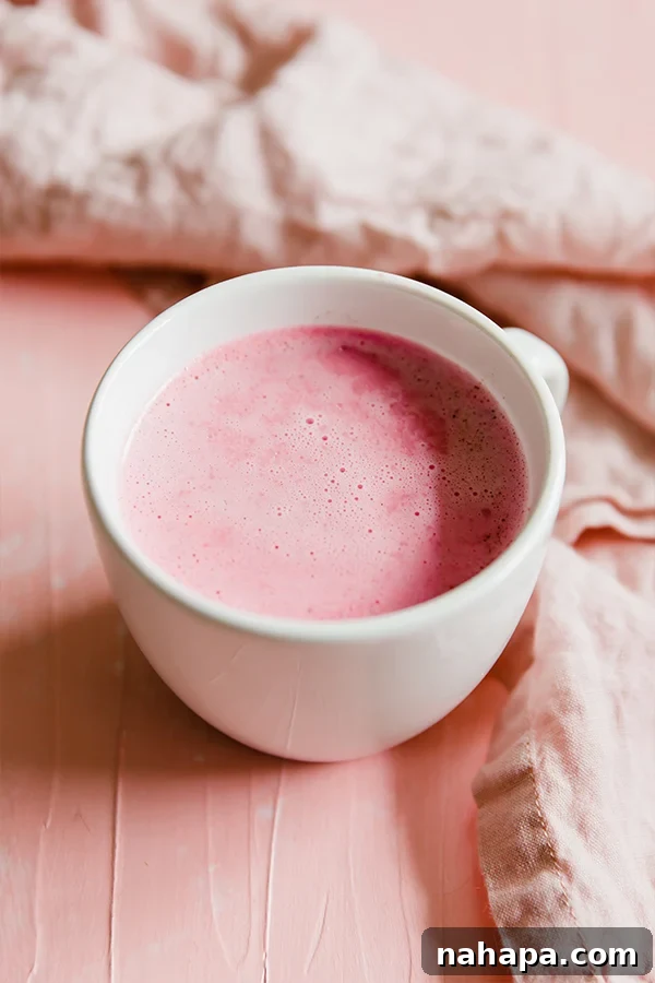 A close-up of a pink beet latte in a mug, with a sprig of a herb for garnish.