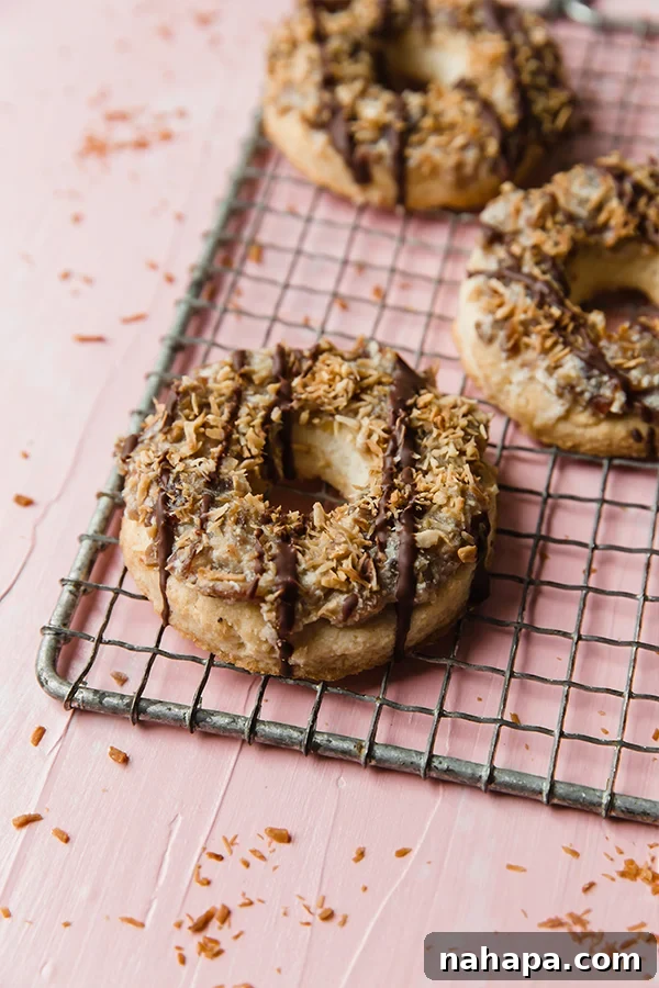 A wire rack with two homemade Samoa cookies, freshly drizzled with chocolate and sprinkled with coconut.