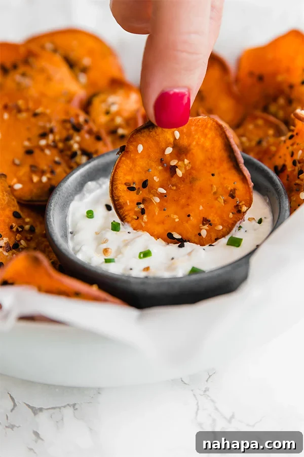 A white plate with sweet potato bagel chips with everything seasoning dipping into a dipping sauce.