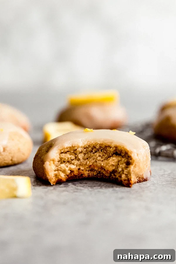 A single Paleo Lemon Cookie with a delicate glaze, perched on a wire cooling rack with lemon slices in the background.