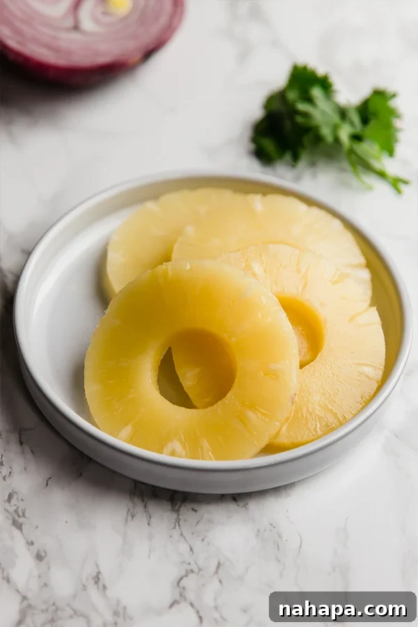 Paleo Whole30 AIP Tropical Teriyaki Chicken Burgers 4 Fresh pineapple slices and red onion ready to be grilled alongside chicken burger patties.