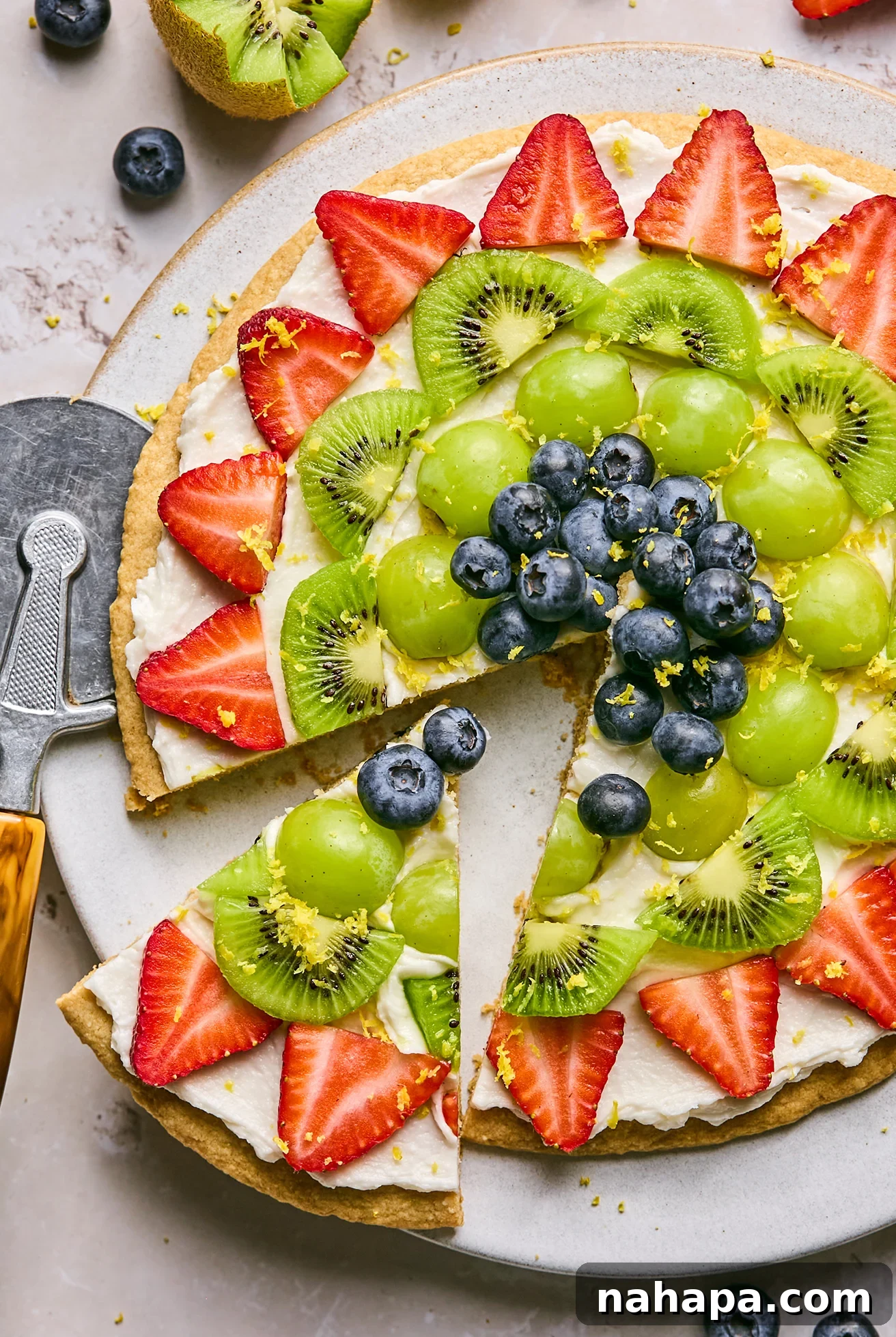 Vibrant Sugar Cookie Fruit Pizza topped with colorful fresh fruit and lemon zest on a large serving platter.