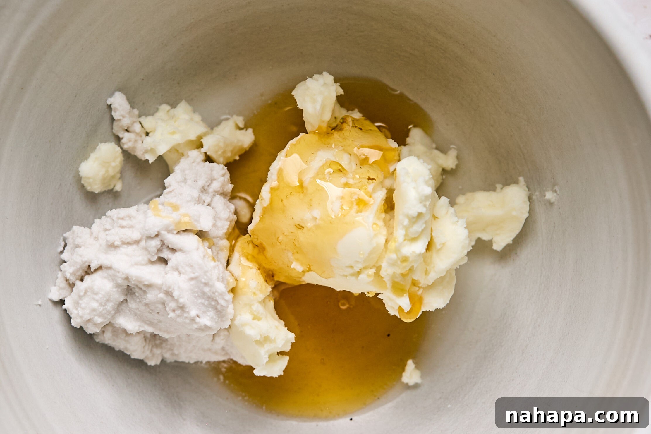 Ingredients for dairy-free frosting being added to a bowl: palm shortening, coconut cream, and honey.