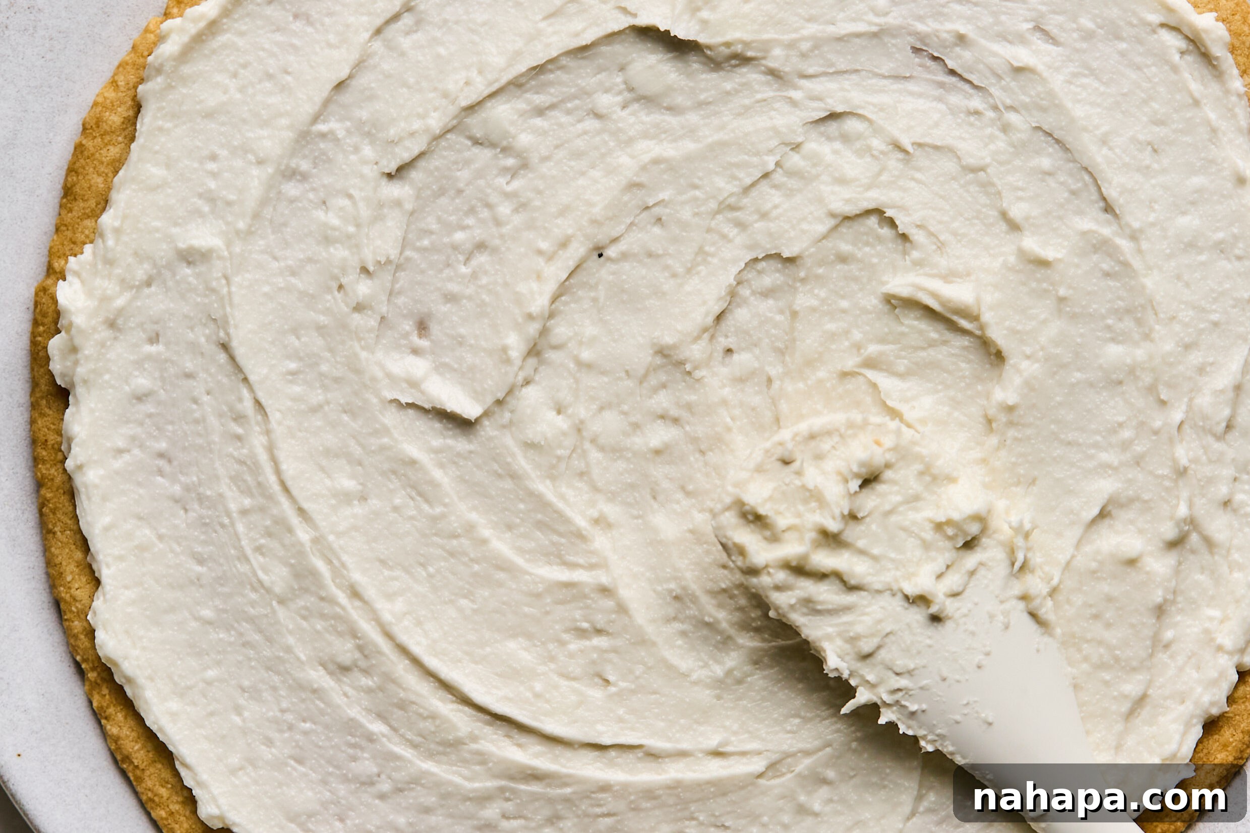 Creamy frosting being spread evenly over the cooled sugar cookie base.