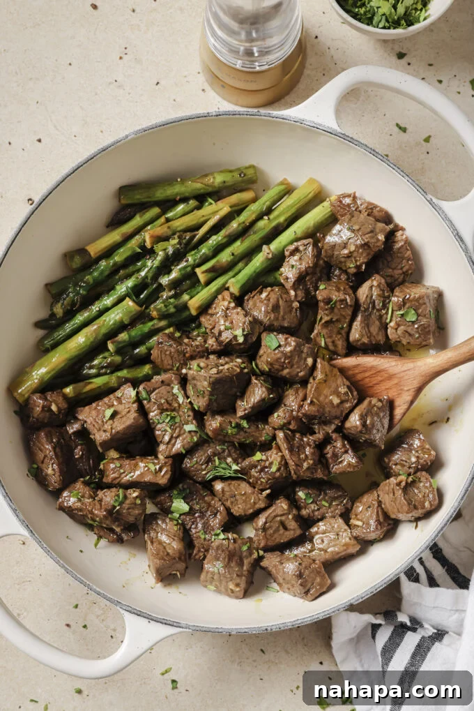 A bowl of Garlic Balsamic Steak Bites with a side of asparagus.