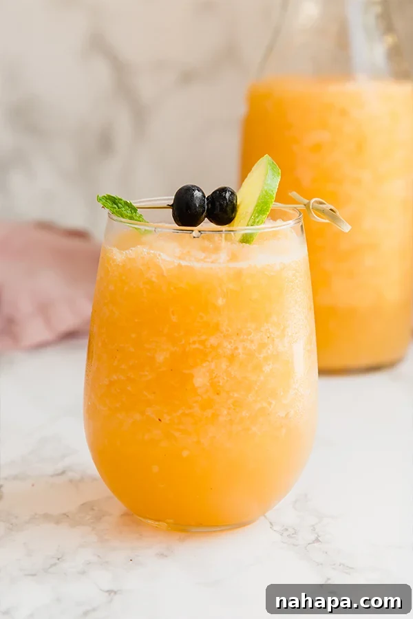 A glass of frozen peach bellini mocktail garnished with fresh mint and berries