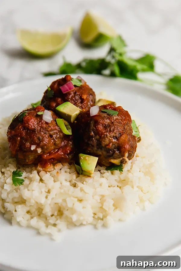 Close-up of enchilada meatballs served over cauliflower rice, garnished with fresh herbs, showcasing the rich sauce and tender texture.