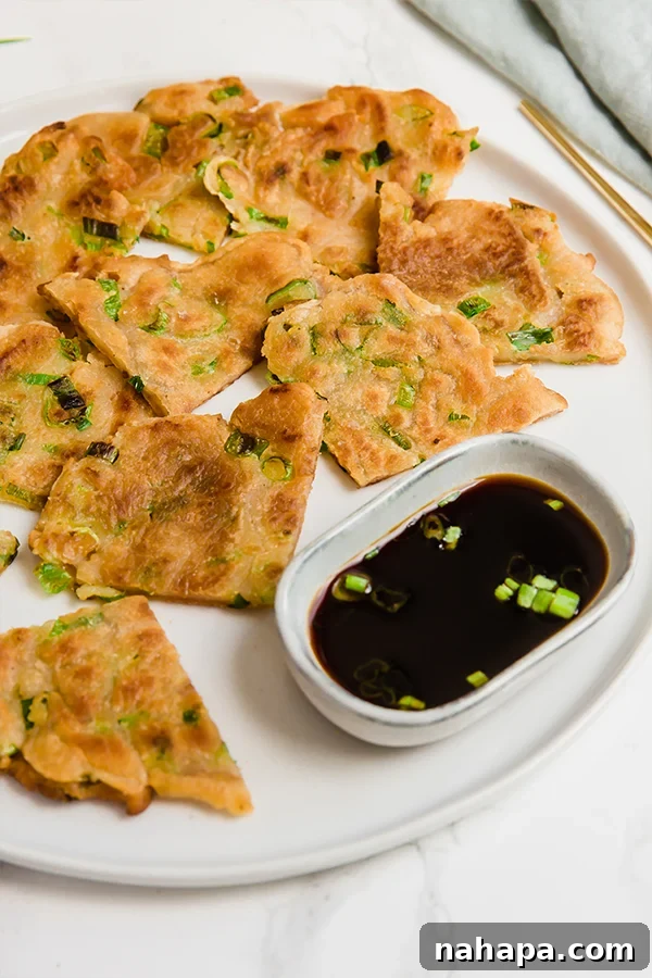 Freshly made gluten-free scallion pancakes stacked on a cutting board, ready to be sliced, showcasing their golden-brown exterior and green flecks of scallions.