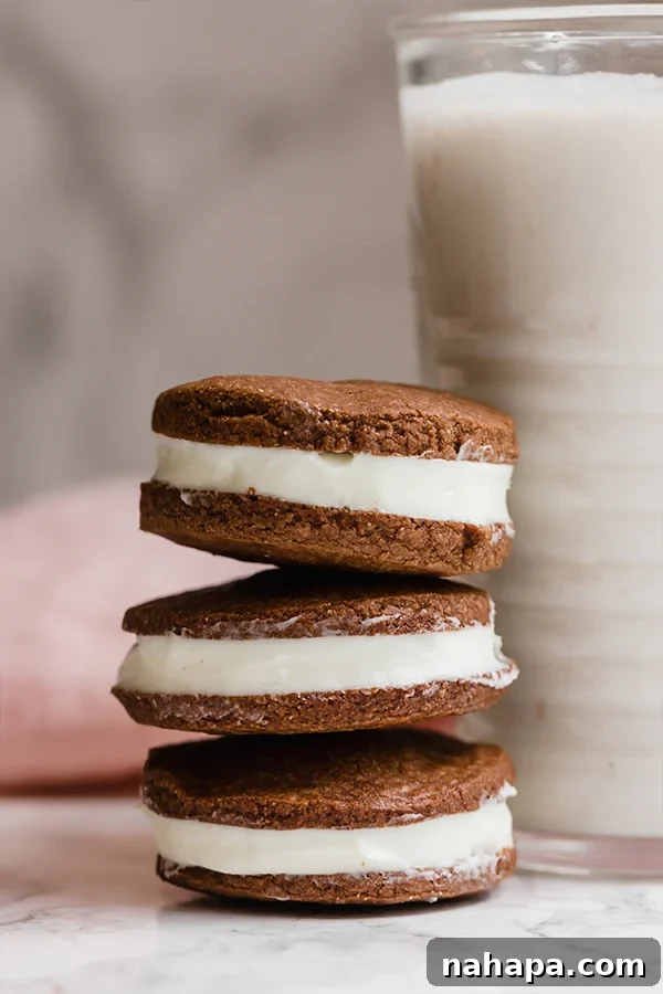 A stack of homemade oreos on top of each other next to a glass of milk.