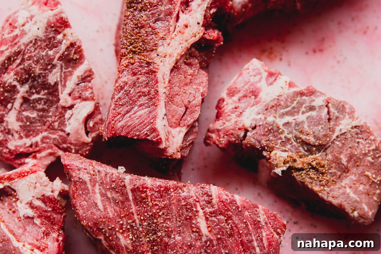 Pieces of raw chuck roast cut into large chunks on a cutting board, seasoned with salt, pepper, and coconut sugar.