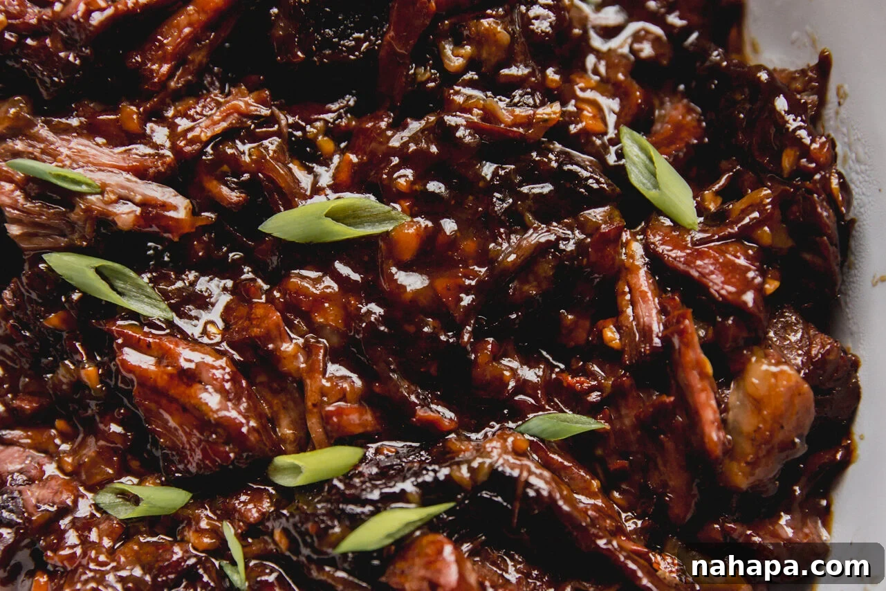 Ginger chuck roast shredded and fully cooked in a large glass dish, topped off with green onion. The meat is visibly tender and moist.