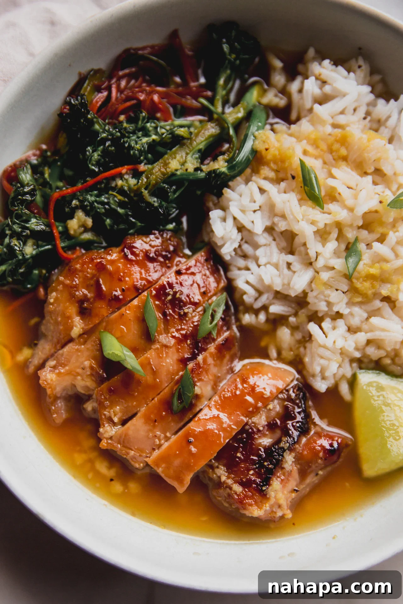 A bowl of sauteed vegetables, sliced chicken thighs, rice, lime and green onion in a ginger broth.