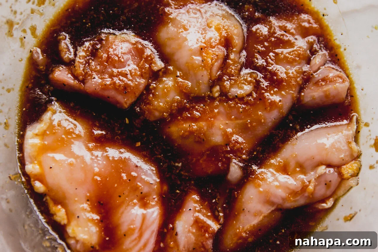 Boneless, skinless chicken thighs marinating in a flavorful sauce in a clear glass bowl, ready for cooking.