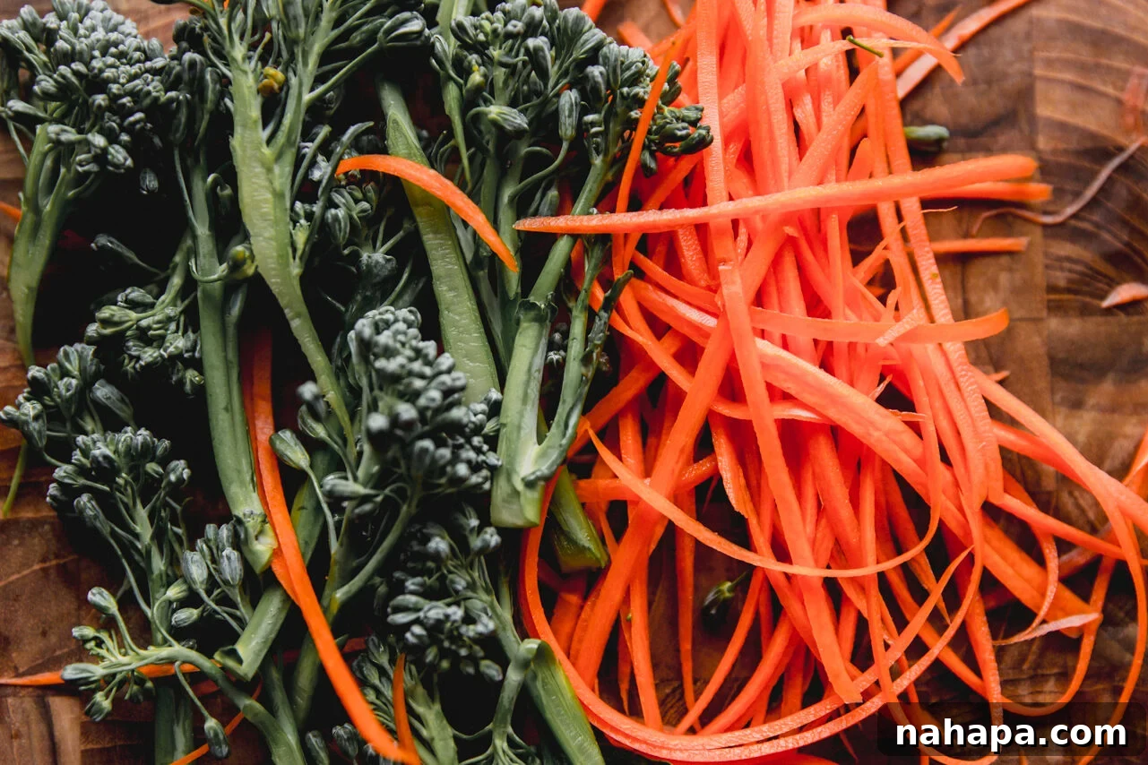 Freshly cut broccoli florets and shredded carrots neatly arranged on a bamboo cutting board, ready for cooking.