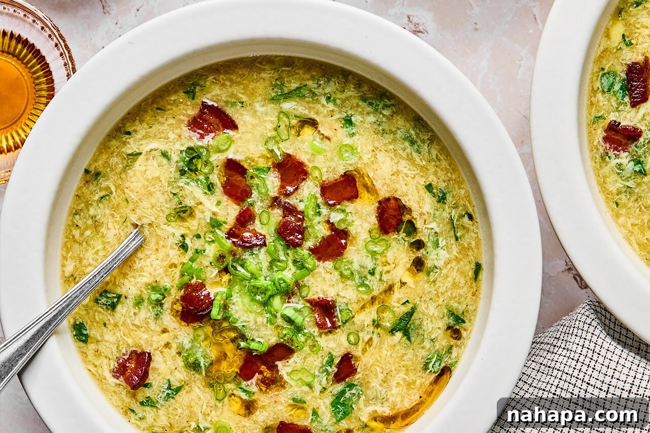 Breakfast egg drop soup in a bowl topped with bacon and green onion, with bacon on the side.