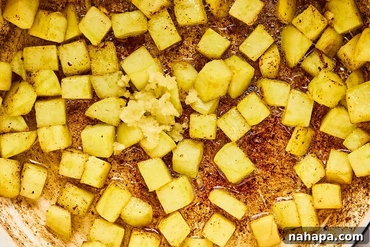 Diced sweet potato sauting in a pan with garlic added on top.