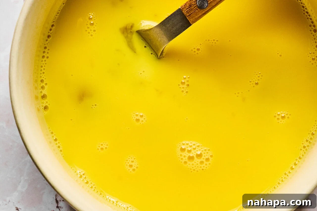 A bowl with eggs whisked with water in it and a fork in it.