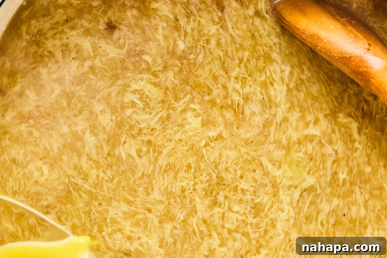 A Dutch oven filled with soup with egg in it and a wooden spoon.