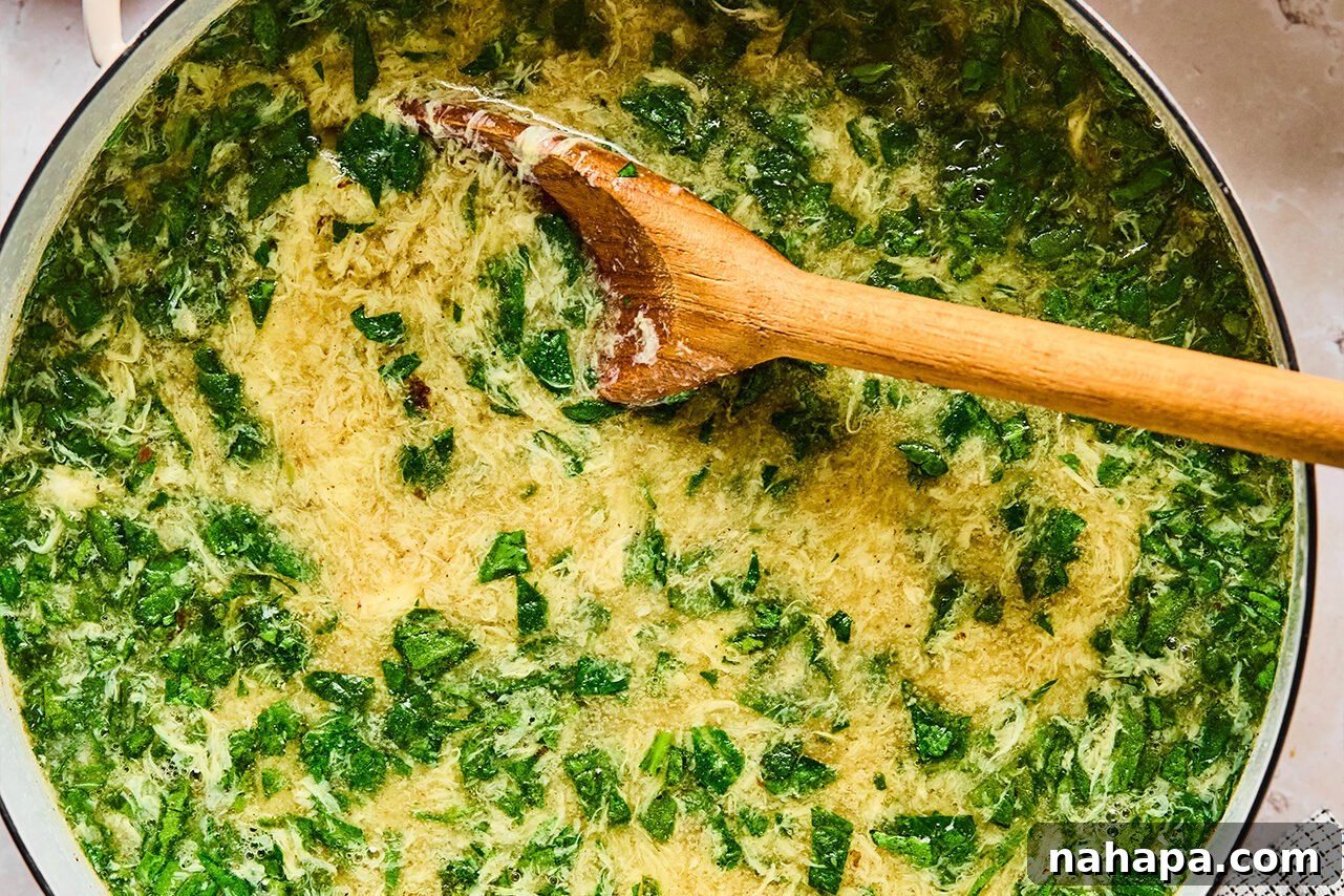 The soup with spinach wilted in it and a wooden spoon stirring it.