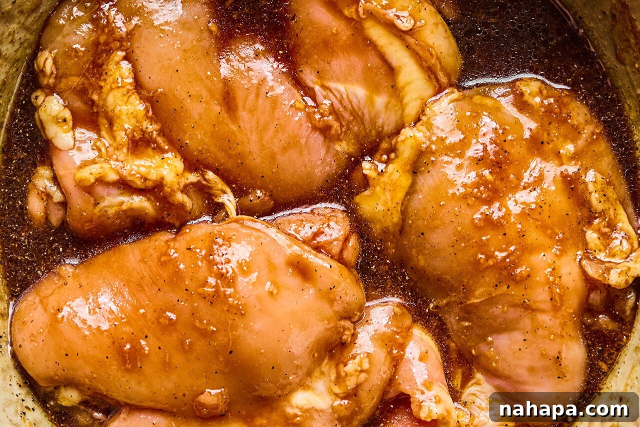 Boneless, skinless chicken thighs marinating in a savory teriyaki sauce in a glass bowl, absorbing all the delicious flavors.