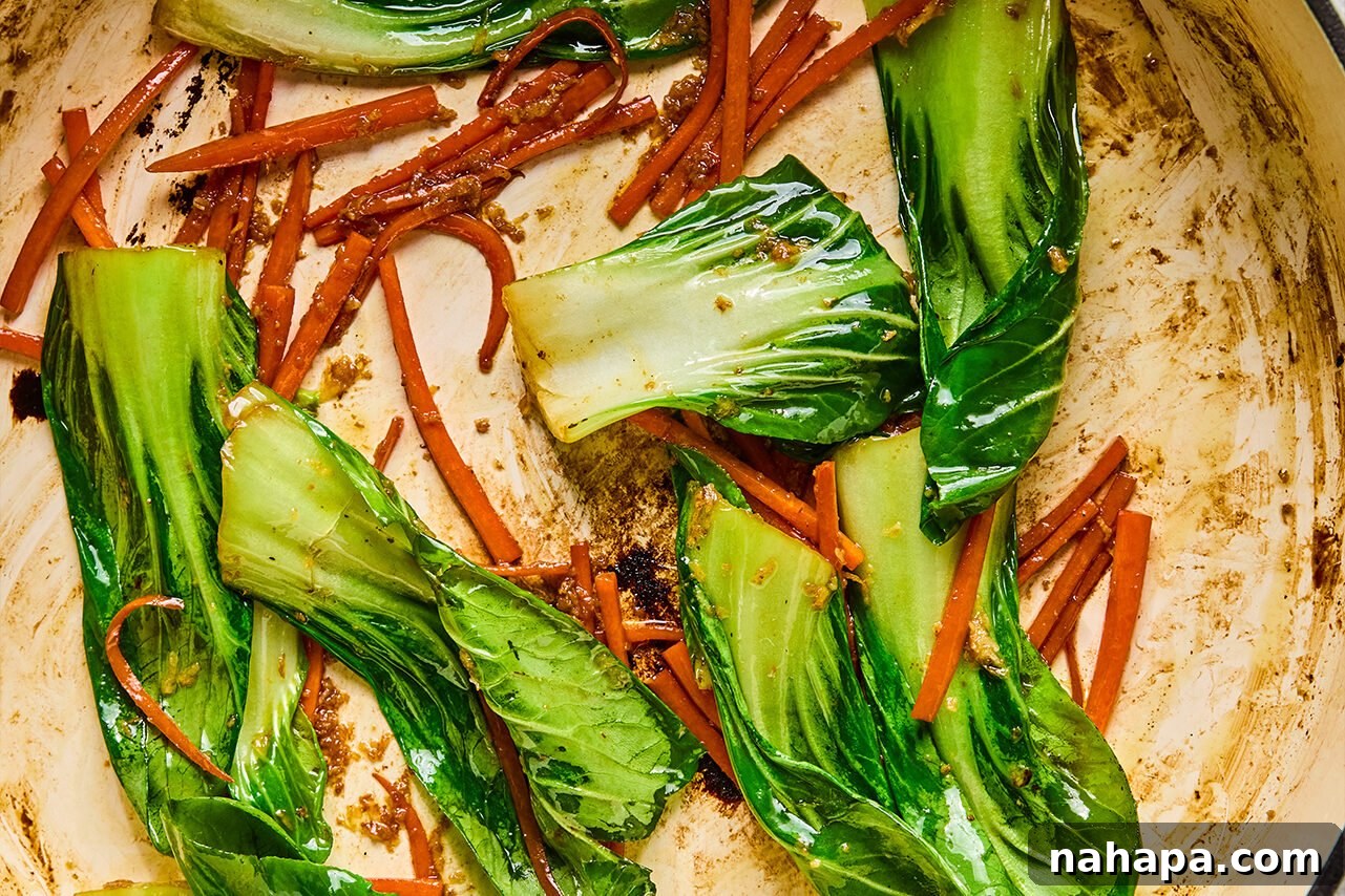 Matchstick carrots and baby bok choy sautéing in a pan with a hint of oil, beginning to soften and release their flavors.