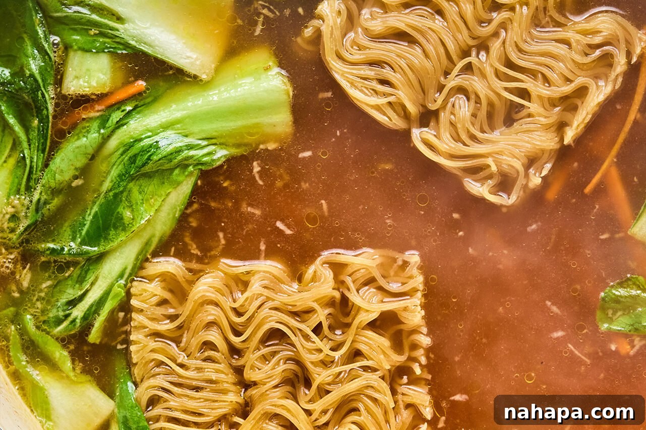 Chicken broth and coconut aminos being poured into a pan containing sautéed carrots and bok choy, ready to form the ramen broth.