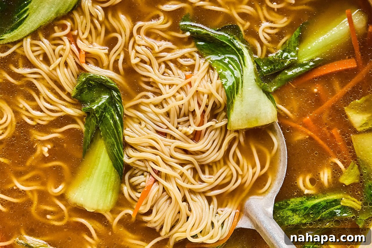 Gluten-free ramen noodles cooking directly in the simmering broth with bok choy and carrots, absorbing the flavors and becoming tender.