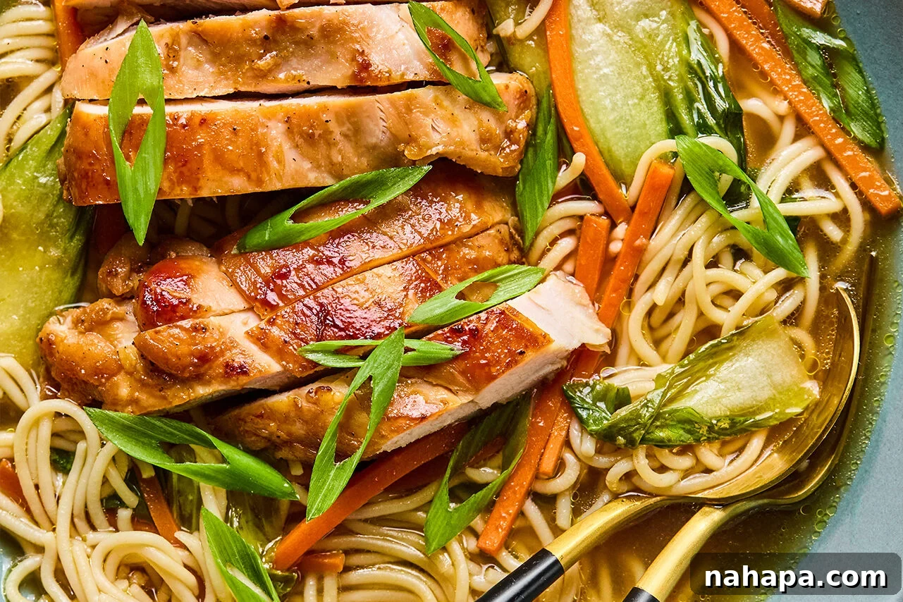 A beautifully assembled bowl of chicken teriyaki ramen, garnished with sliced chicken, green onions, and a perfectly placed spoon, ready to be enjoyed.