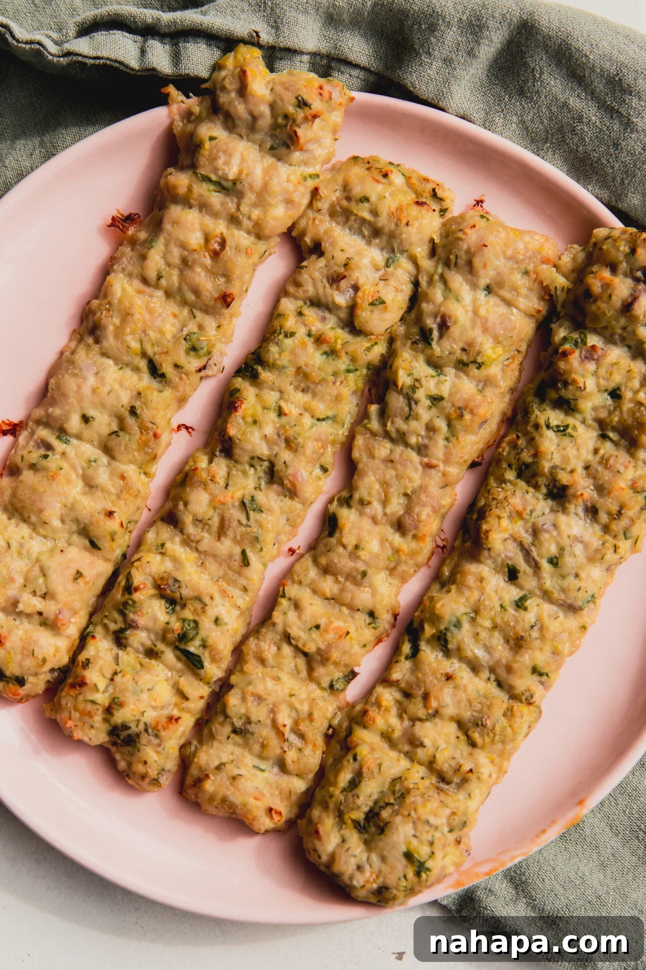 Four sheet pan chicken kebabs on a pink plate, garnished with fresh herbs.