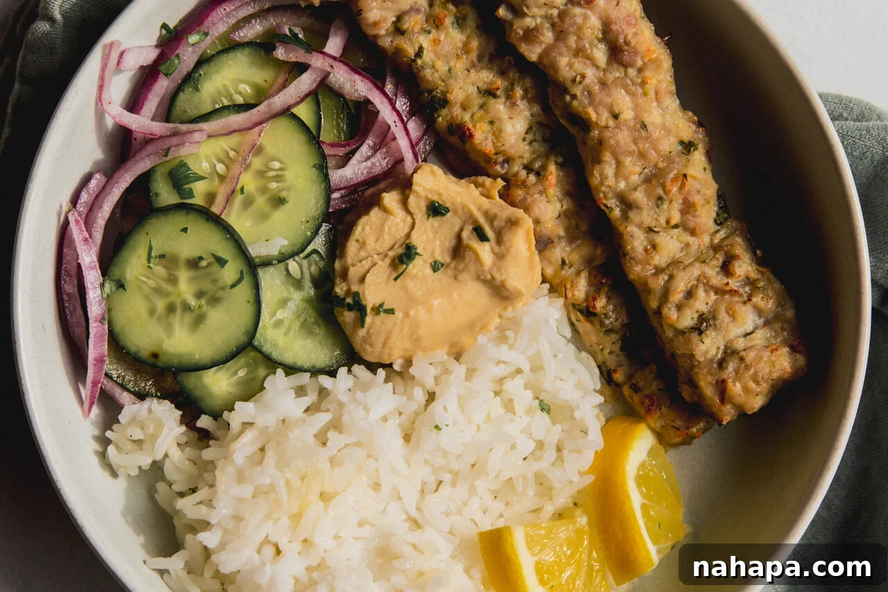 Two sheet pan kebabs in a bowl, served alongside a refreshing cucumber salad, fluffy white rice, and bright sliced lemon wedges.