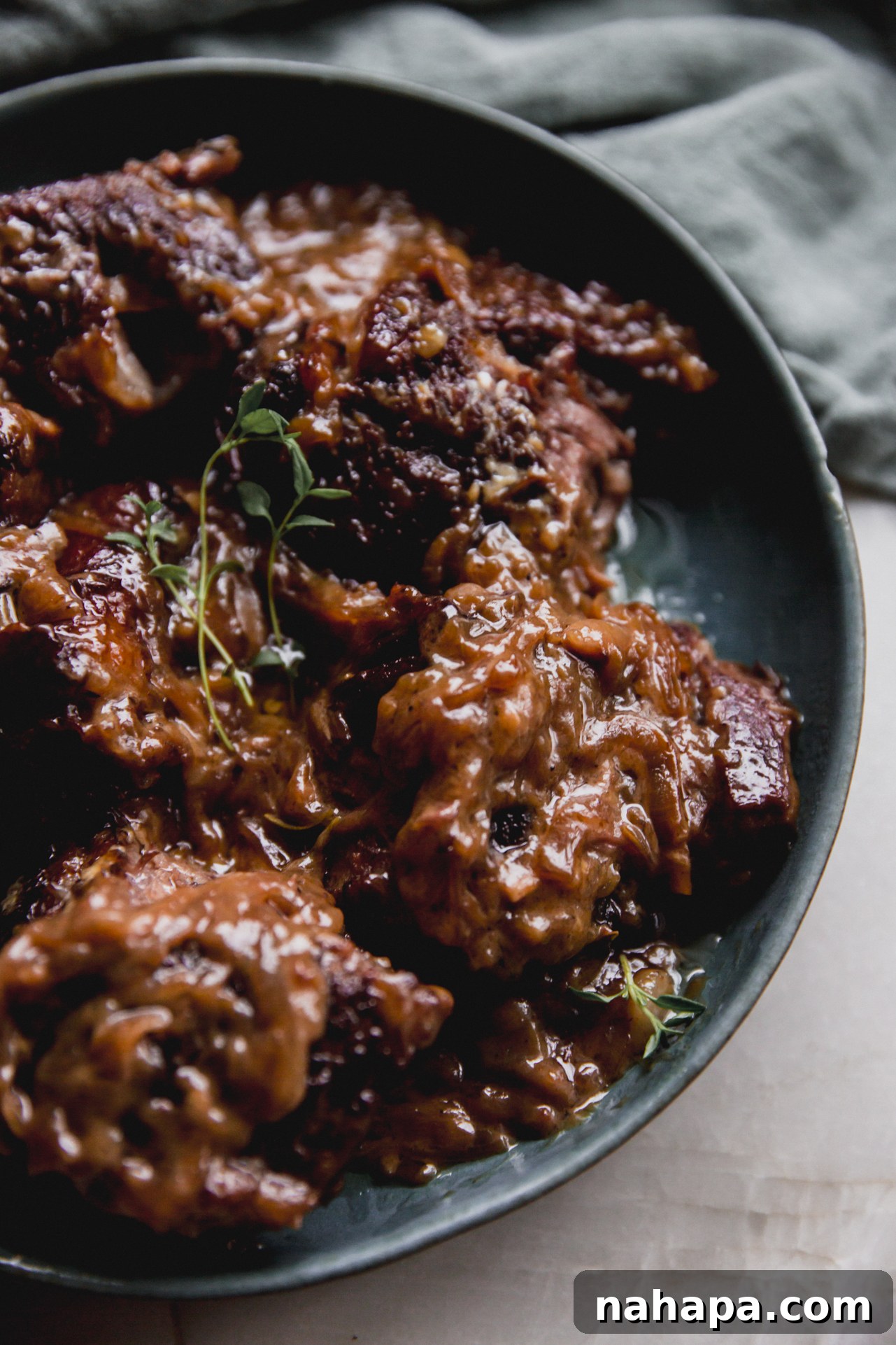 French onion short ribs in a green bowl, shredded and topped with fresh thyme.