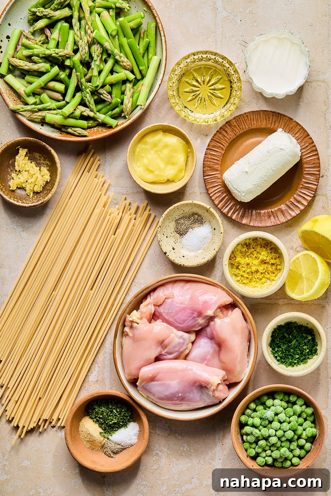 Bright Lemon Goat Cheese Pasta 4 All the ingredients to make lemon goat cheese pasta in bowls on a counter before cooking, including chicken, asparagus, peas, lemon, garlic, and cheese.
