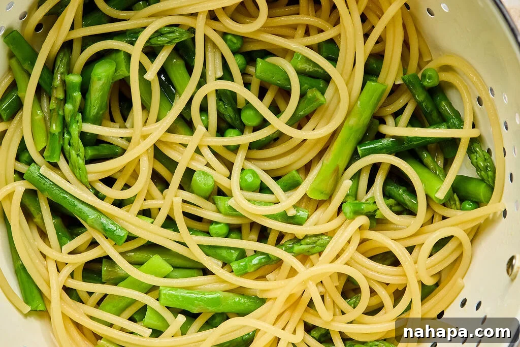 Bright Lemon Goat Cheese Pasta 8 A strainer filled with cooked gluten-free bucatini, vibrant green peas, and tender asparagus after draining.