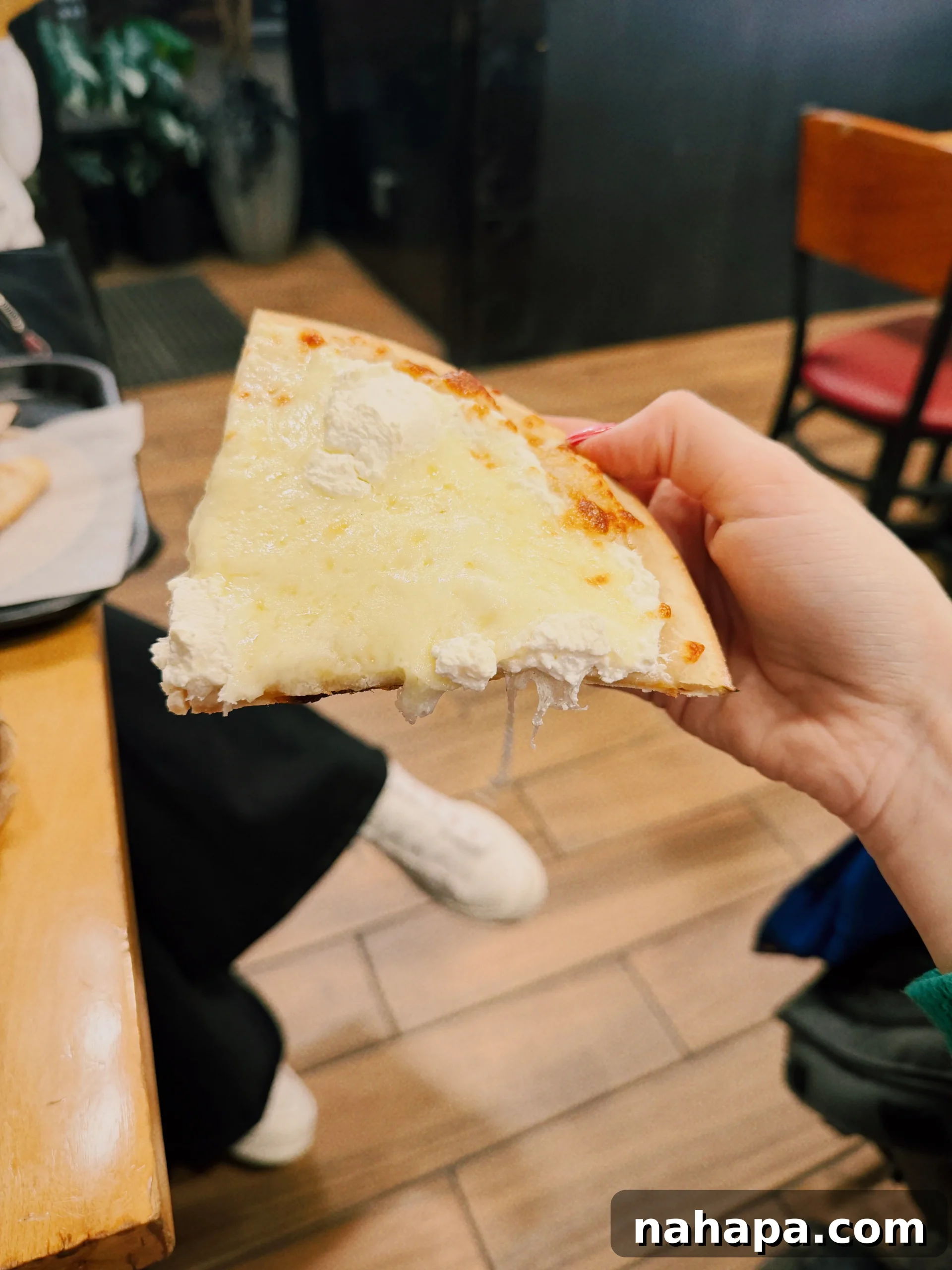 My Gluten-Free and Nightshade-Free NYC Food Guide 9 A mouth-watering slice of white pizza with a perfectly crispy crust being held up, showcasing the melted cheese and fresh herbs.
