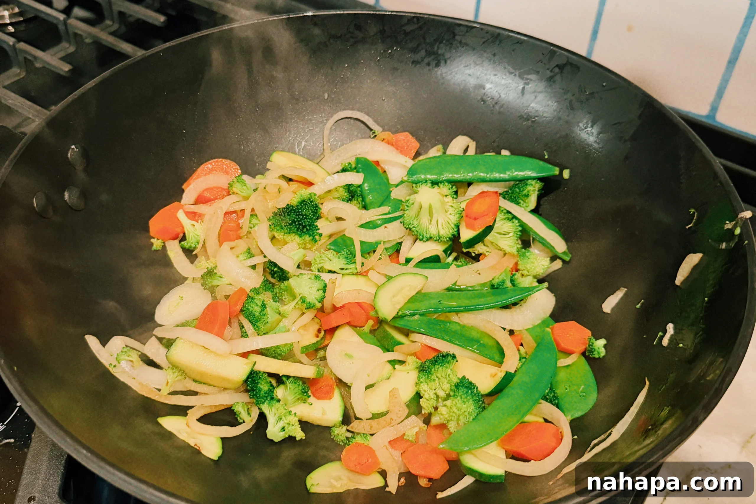 A vibrant mix of sliced yellow onions, snow peas, broccoli florets, chopped zucchini, and thin carrot slices actively stir-frying in a large black wok over high heat, showing light charring on some pieces.