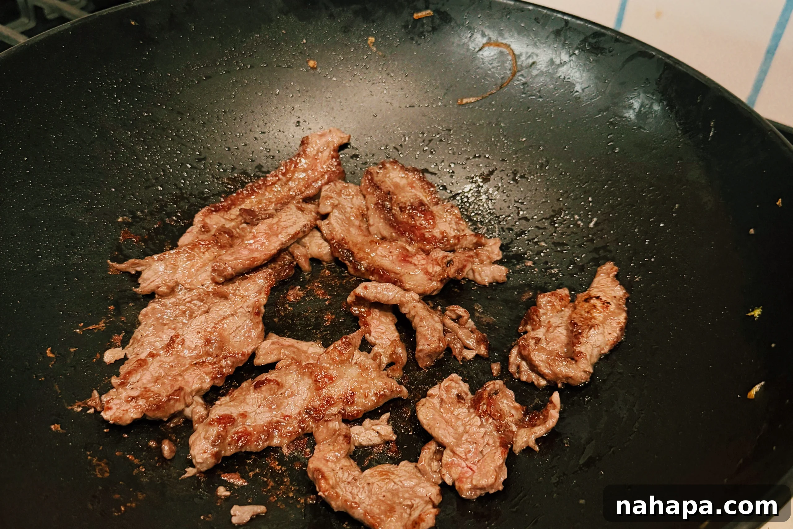 Thin strips of marinated flank steak sizzling and browning in a hot black wok, spread in a single layer to ensure even cooking and a crispy exterior.
