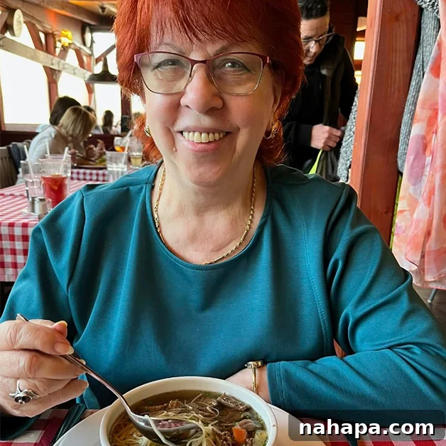 A lovely woman with red hair and a blue shirt enjoying a bowl of soup, an example of traditional bone broth consumption.