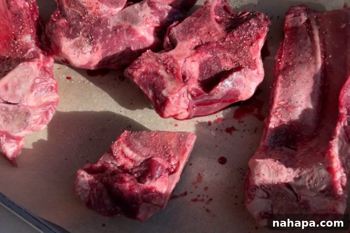 Meaty beef bones arranged on a parchment-lined baking sheet, seasoned and ready for roasting.